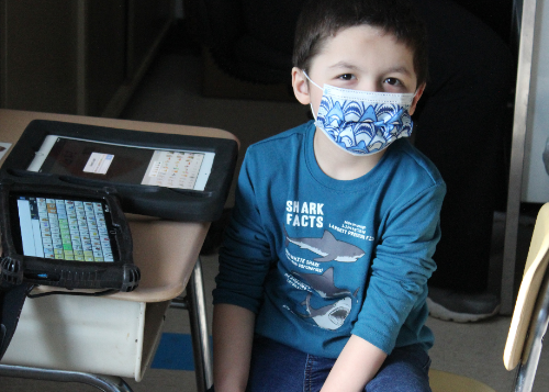 Smiling student wearing mask sitting at desk with assistive device