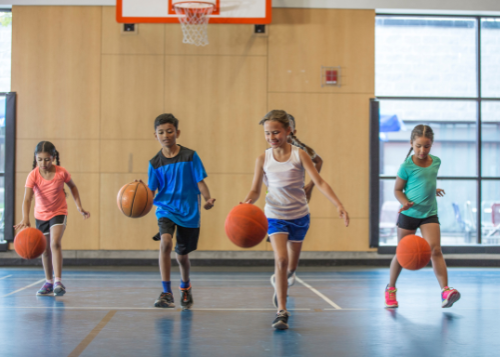 Four children playing basketball in a gymnasium.