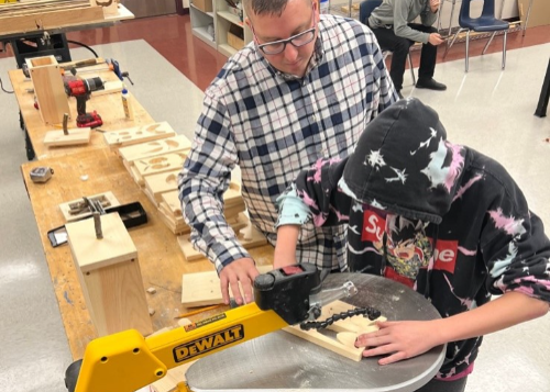 Teacher assisting student using power equipment