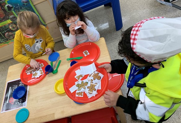 Three preschoolers pretending to make and eat gingerbread cookies