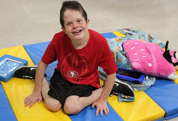 Smiling student sitting on blue and yellow gym pad