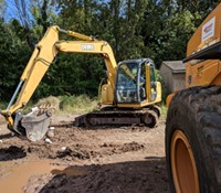 A student operates an excavator, preparing to scoop soil. 