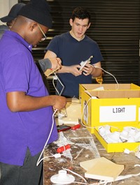 Two students stand at a table adding wires to light fixture bases